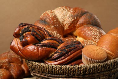 Wicker basket with different tasty freshly baked pastries on brown background, closeup