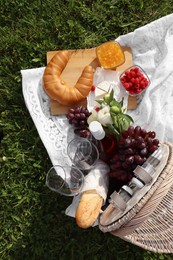 Photo of Picnic blanket with tasty food, flowers, basket and cider on green grass outdoors, flat lay