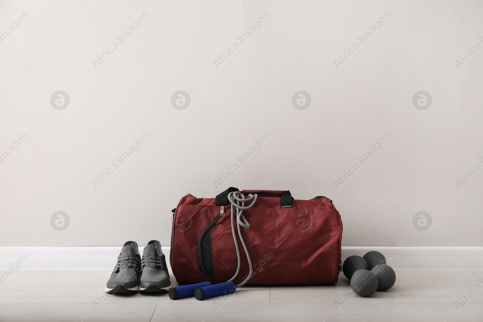 Photo of Red bag and sports accessories on floor near light wall, space for text