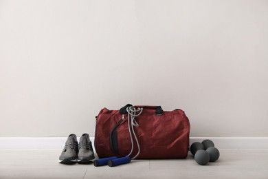 Photo of Red bag and sports accessories on floor near light wall, space for text