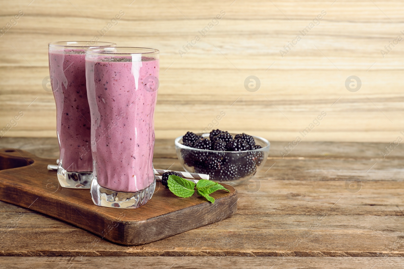 Photo of Delicious blackberry smoothie in glasses on wooden table. Space for text