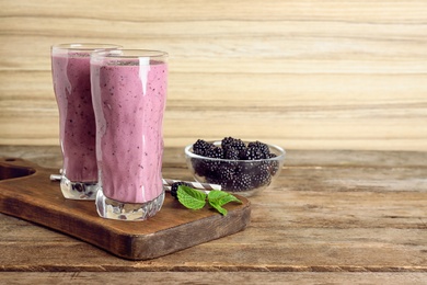 Delicious blackberry smoothie in glasses on wooden table. Space for text