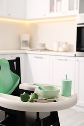 Photo of High chair with broccoli and set of baby tableware on tray indoors