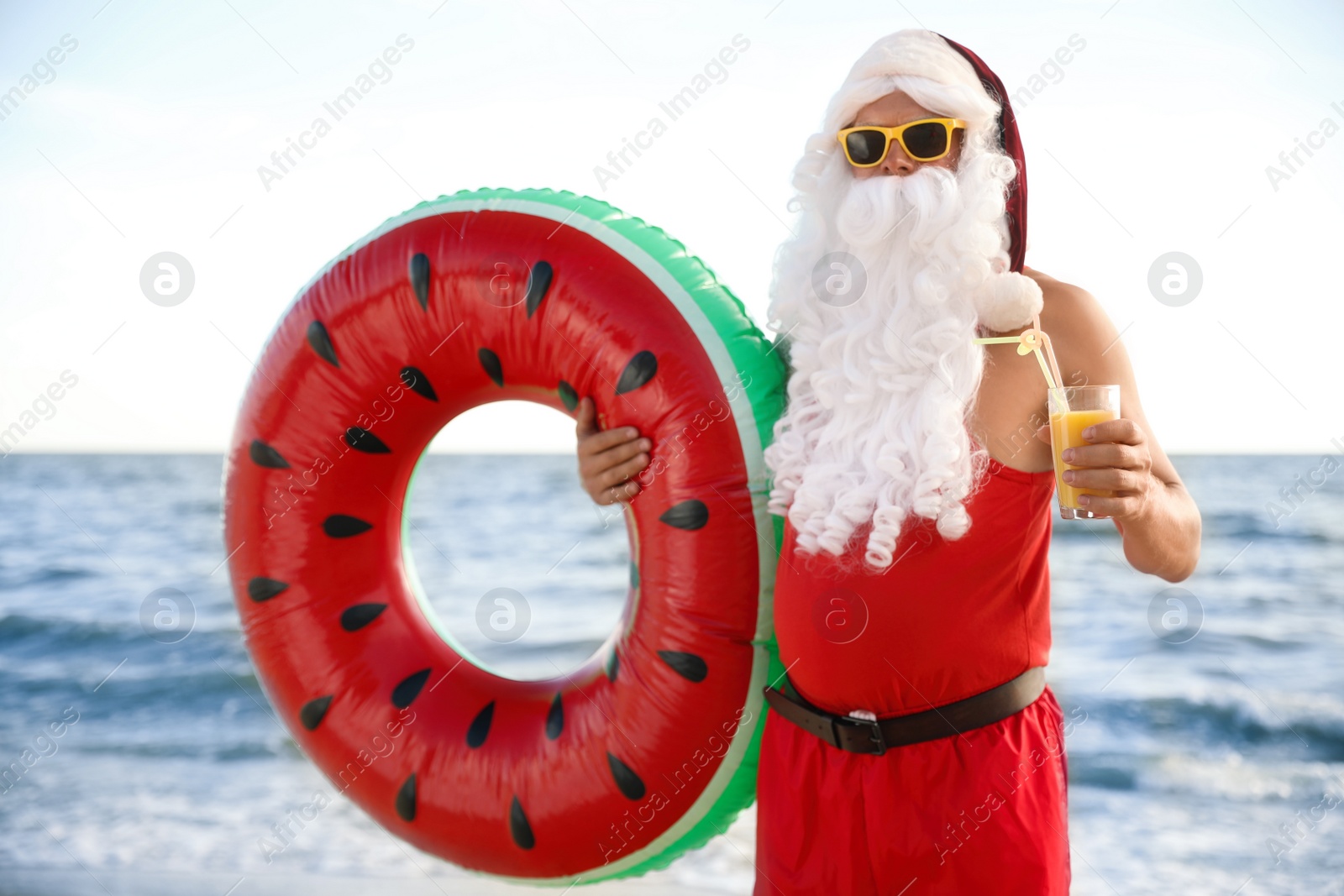Photo of Santa Claus with cocktail and inflatable ring on beach. Christmas vacation
