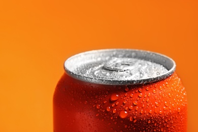 Aluminum can of beverage covered with water drops on orange background, closeup. Space for text