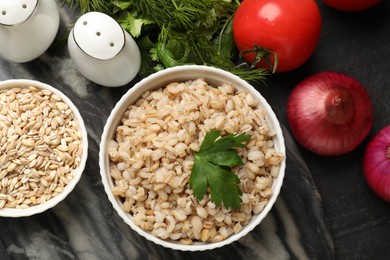 Photo of Tasty pearl barley porridge and parsley in bowl on dark textured table, flat lay