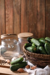 Photo of Fresh cucumbers and other ingredients near empty jars prepared for canning on wooden table