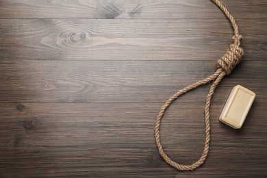 Photo of Rope noose and soap bar on wooden table, flat lay. Space for text