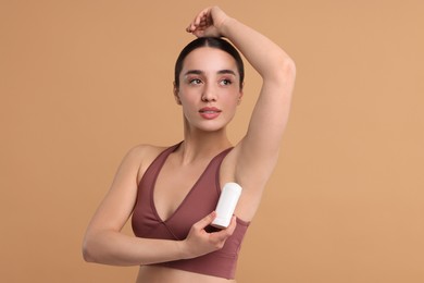 Photo of Beautiful woman applying deodorant on beige background