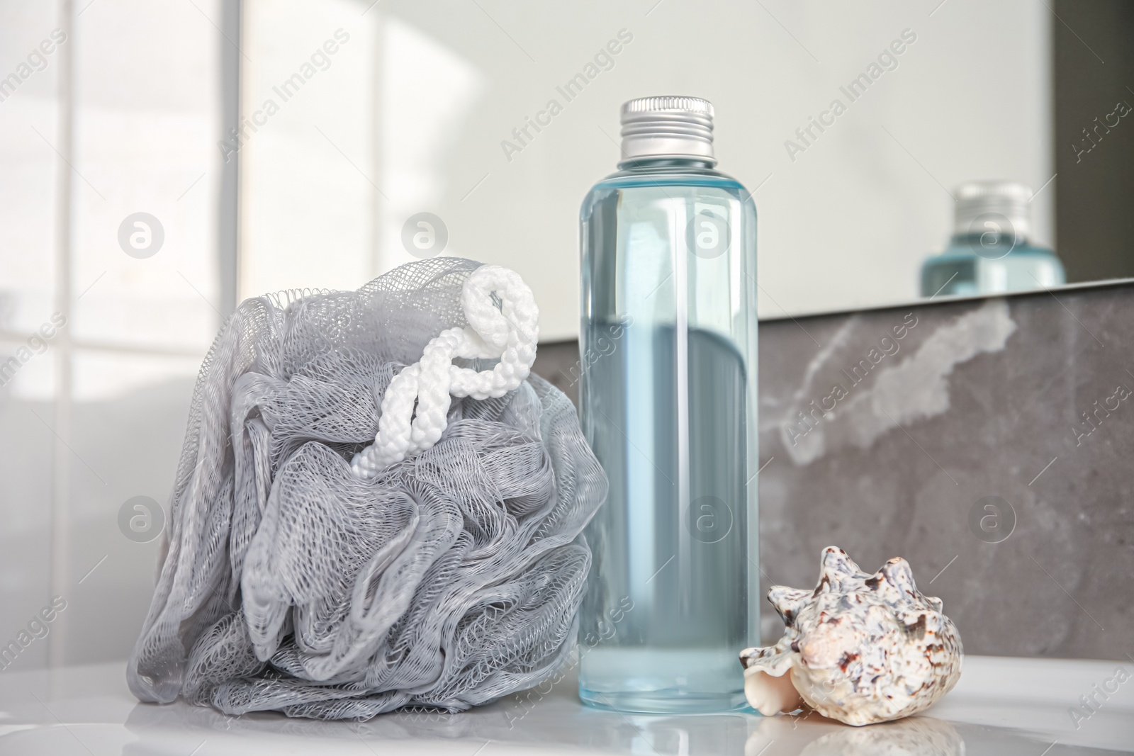 Photo of Grey sponge, seashell and shower gel bottle on washbasin in bathroom