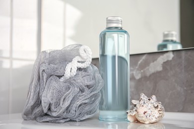 Grey sponge, seashell and shower gel bottle on washbasin in bathroom