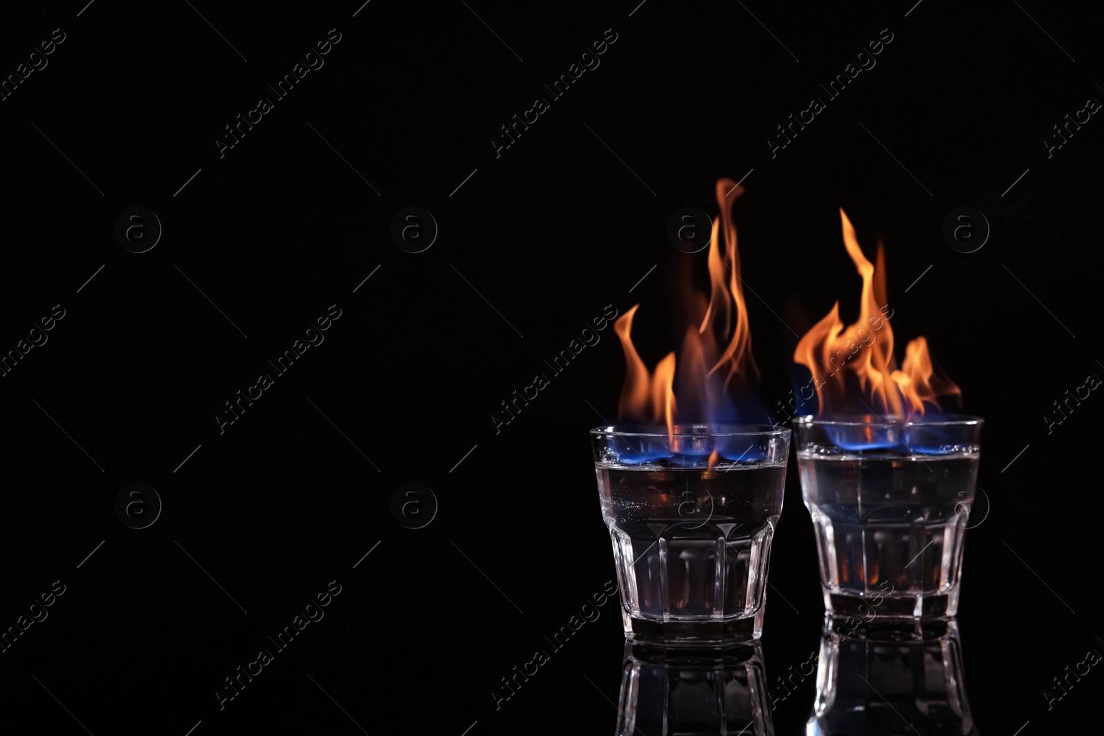 Photo of Flaming vodka in shot glasses on black background, space for text