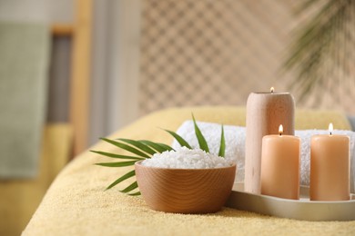 Photo of Spa composition. Burning candles, sea salt and towel on soft yellow surface, space for text