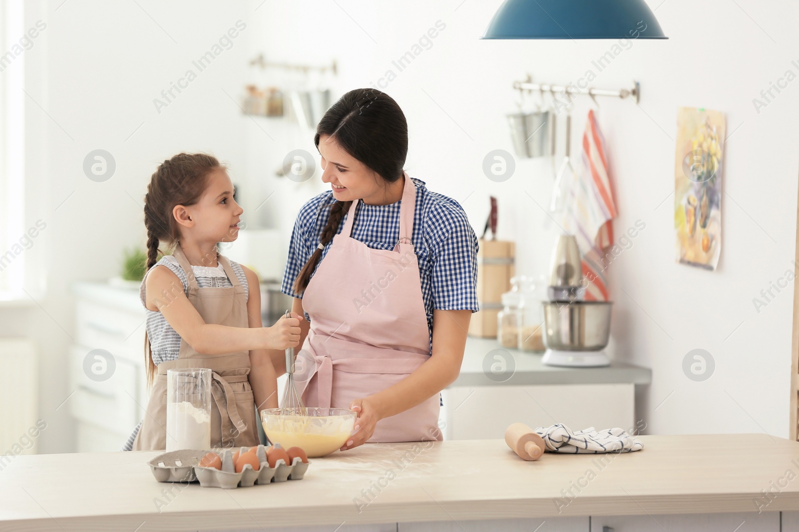 Photo of Mother and her daughter making dough at table in kitchen