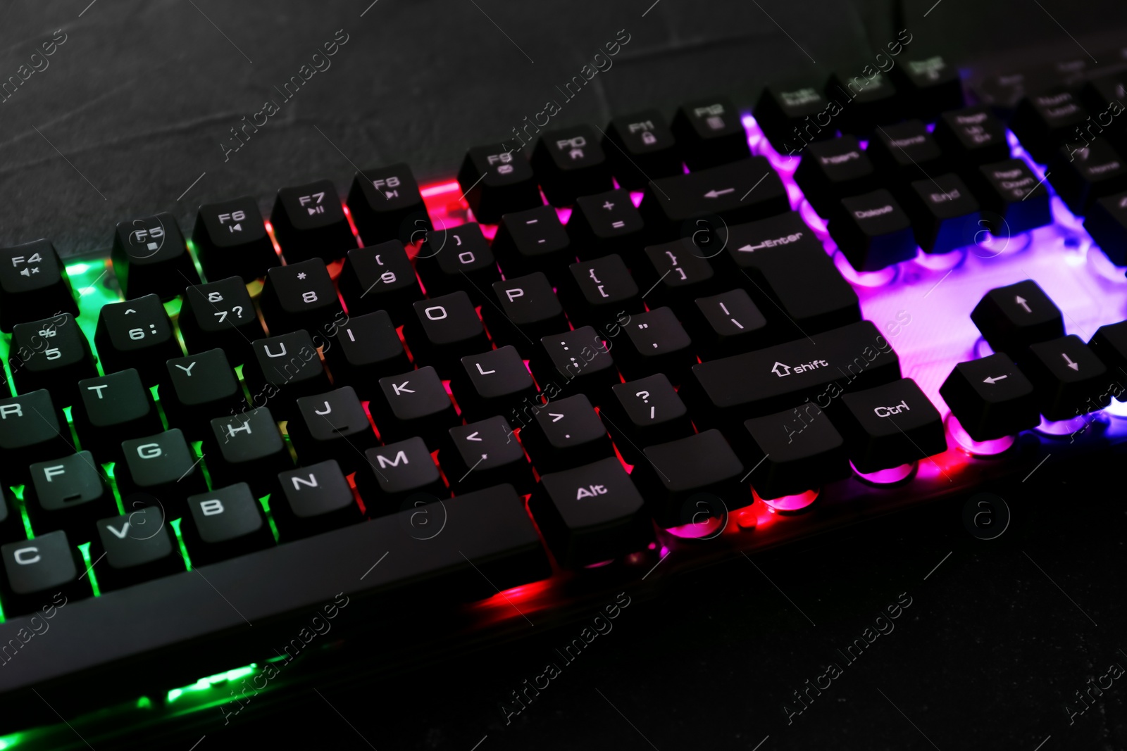 Photo of Modern keyboard with RGB lighting on black table, closeup