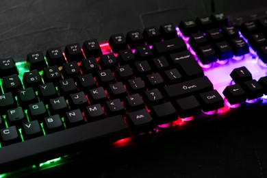 Photo of Modern keyboard with RGB lighting on black table, closeup