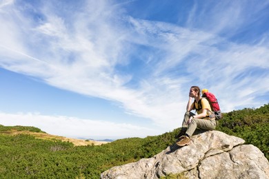 Image of Young woman with backpack on rocky cliff in mountains