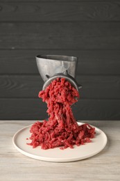 Metal meat grinder with beef mince on light wooden table