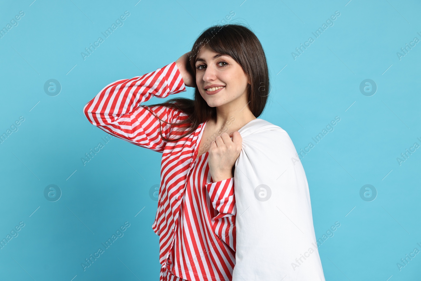 Photo of Happy woman wearing pyjama and holding blanket on light blue background