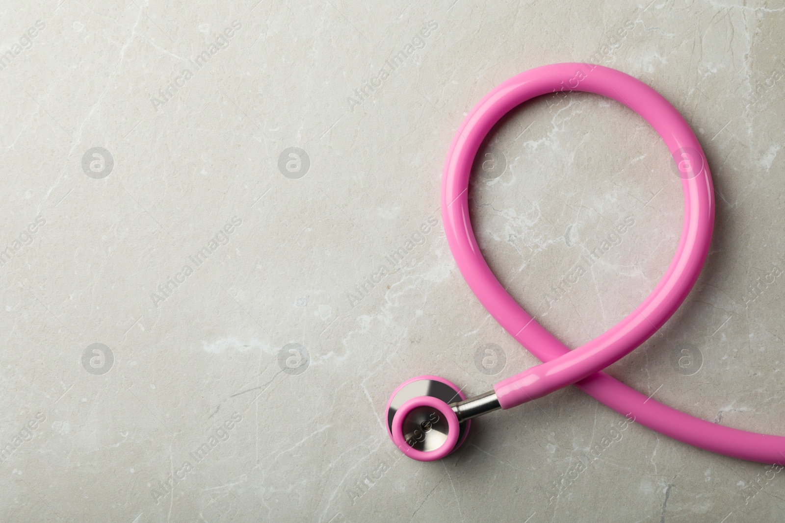 Photo of Pink stethoscope folded like awareness ribbon on grey background, top view with space for text. Breast cancer concept