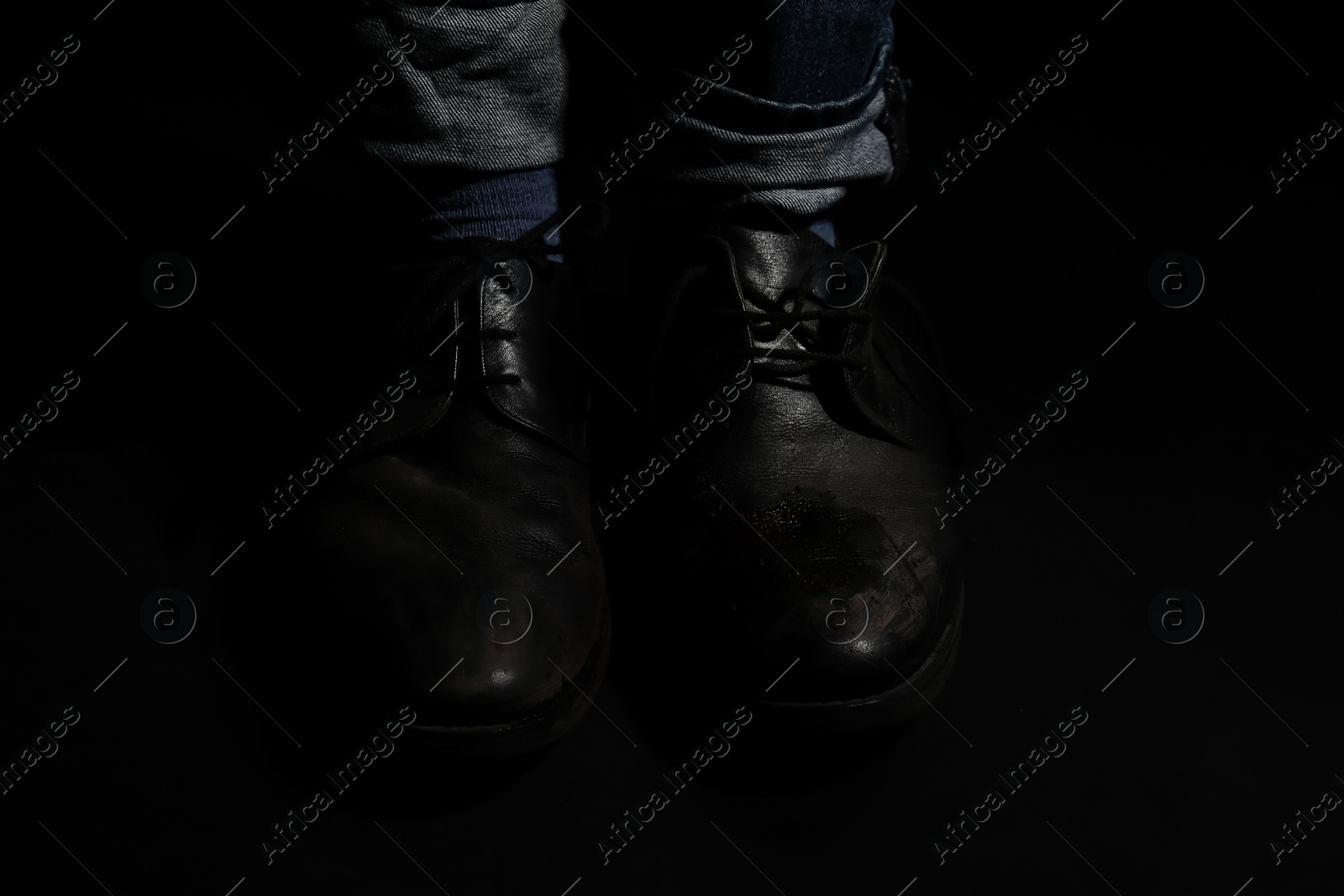 Photo of Poor man in dirty shoes on dark background, closeup