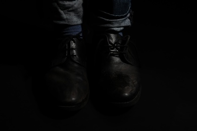 Photo of Poor man in dirty shoes on dark background, closeup