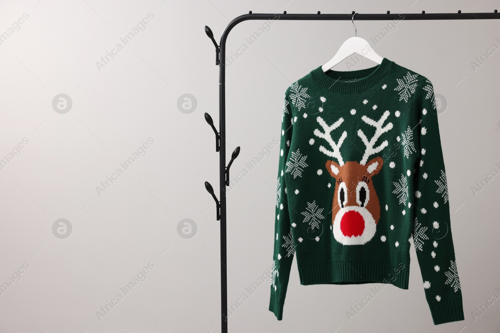 Photo of Rack with Christmas sweater on light background, space for text