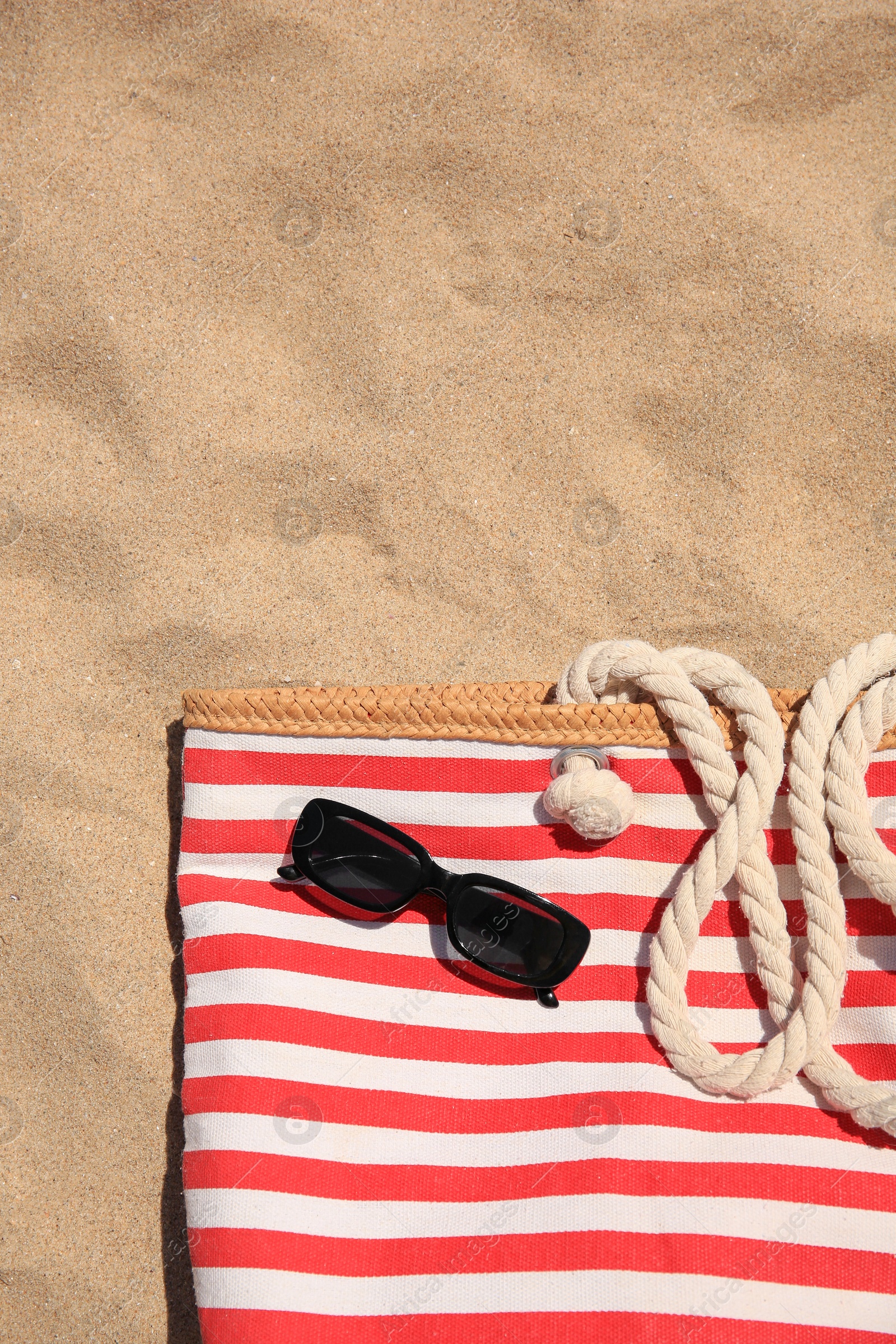 Photo of Striped beach bag and sunglasses on sand, top view. Space for text