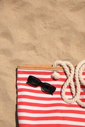 Photo of Striped beach bag and sunglasses on sand, top view. Space for text