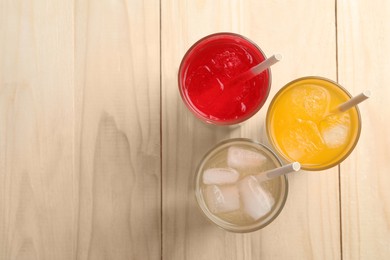 Photo of Glasses of different refreshing soda water with ice cubes and straws on wooden table, flat lay. Space for text