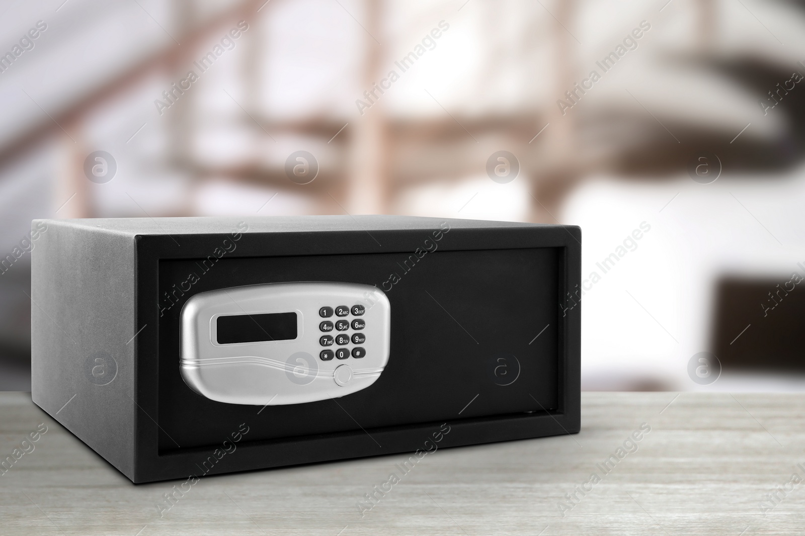 Image of Closed black steel safe with electronic lock on white wooden table indoors