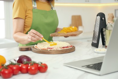 Woman making pizza while watching online cooking course via laptop in kitchen, closeup