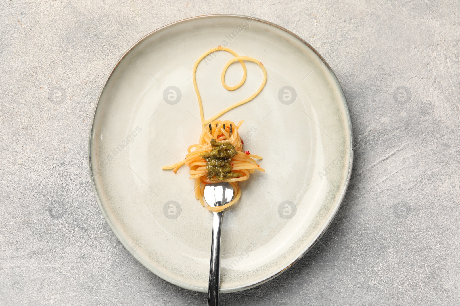 Photo of Heart made with spaghetti and fork on grey table, top view