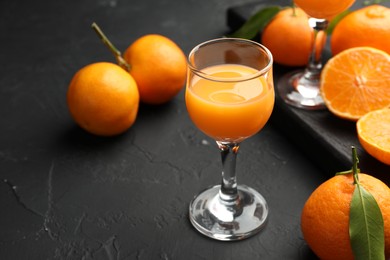 Photo of Tasty tangerine liqueur in glasses and fresh citrus fruits on black textured table