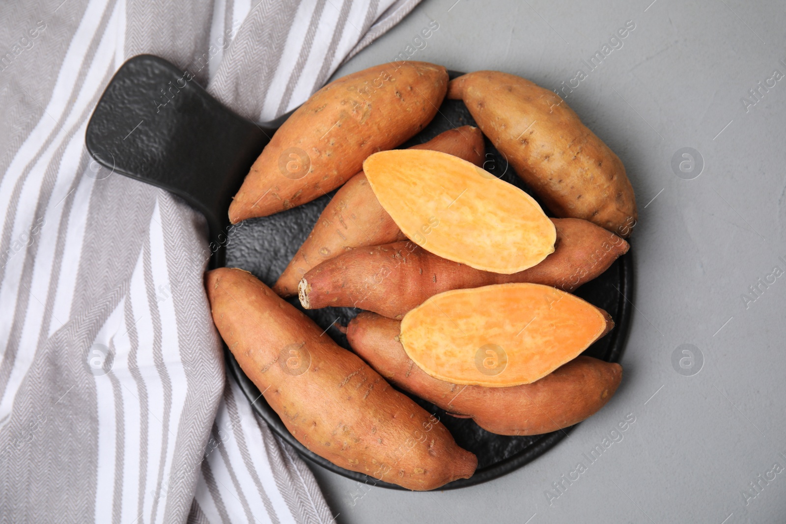 Photo of Slate board with cut and whole sweet potatoes on light grey table, top view