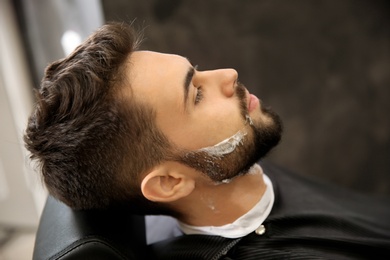 Photo of Young man with shaving foam on face in barbershop. Professional service