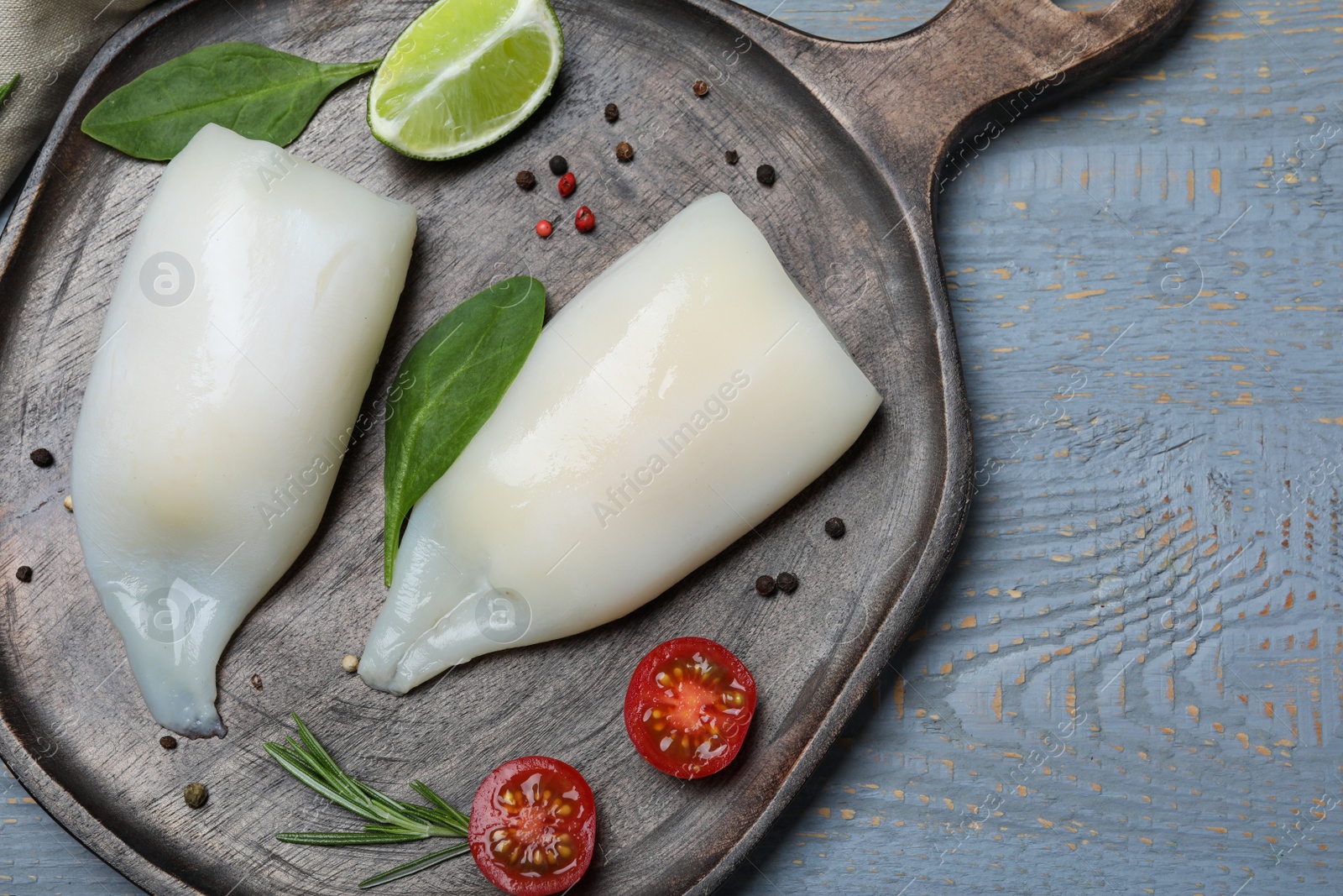 Photo of Fresh raw squid tubes with lime, herbs and tomato on grey wooden table, top view