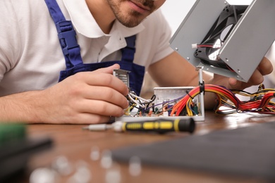 Photo of Male technician repairing power supply unit at table, closeup