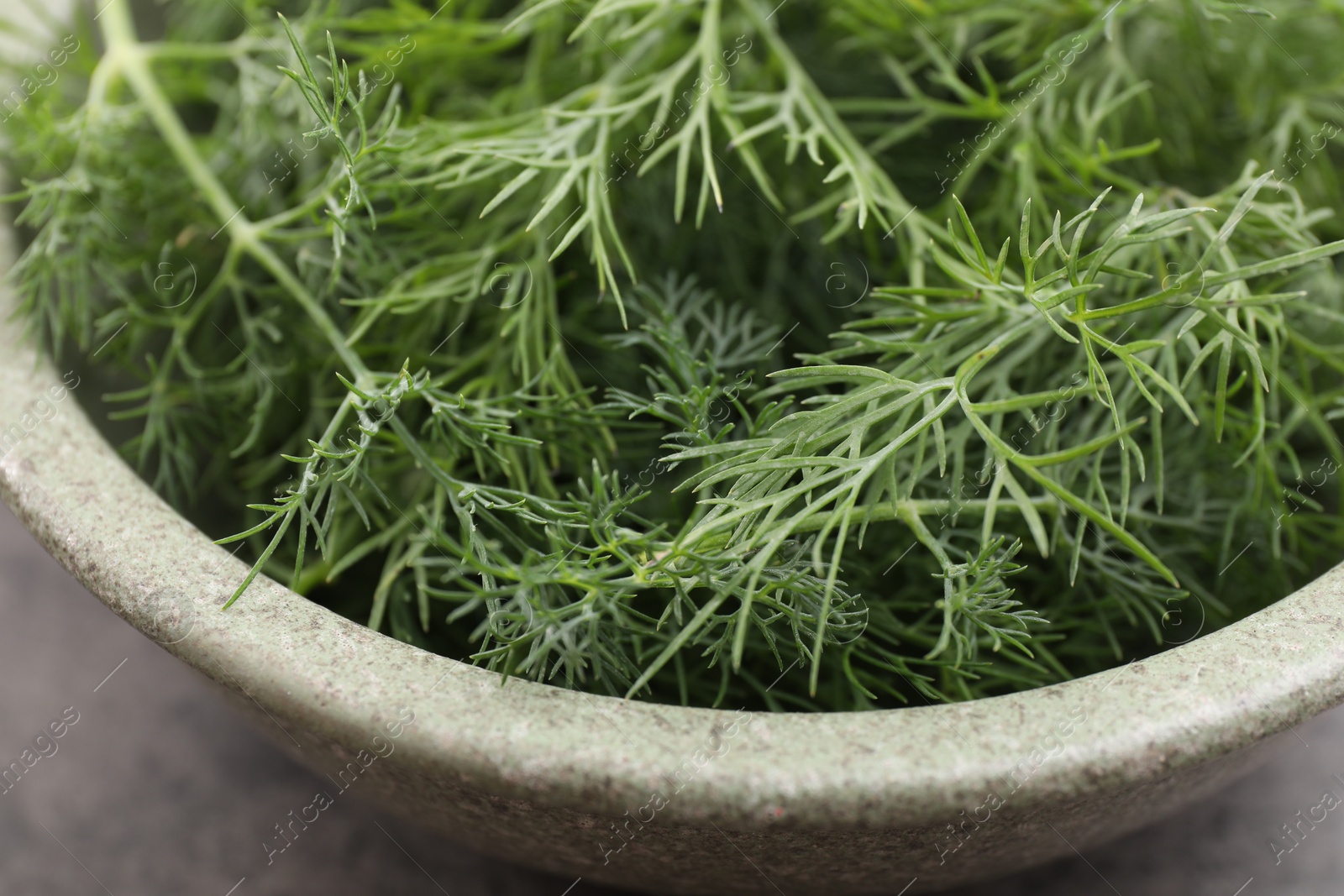 Photo of Bowl of fresh dill on grey table, closeup