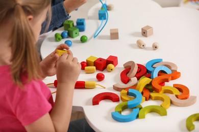 Photo of Little children playing with wooden pieces and string for threading activity at white table indoors, closeup. Developmental toys