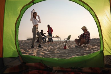 Photo of Friends resting on sandy beach, view from camping tent