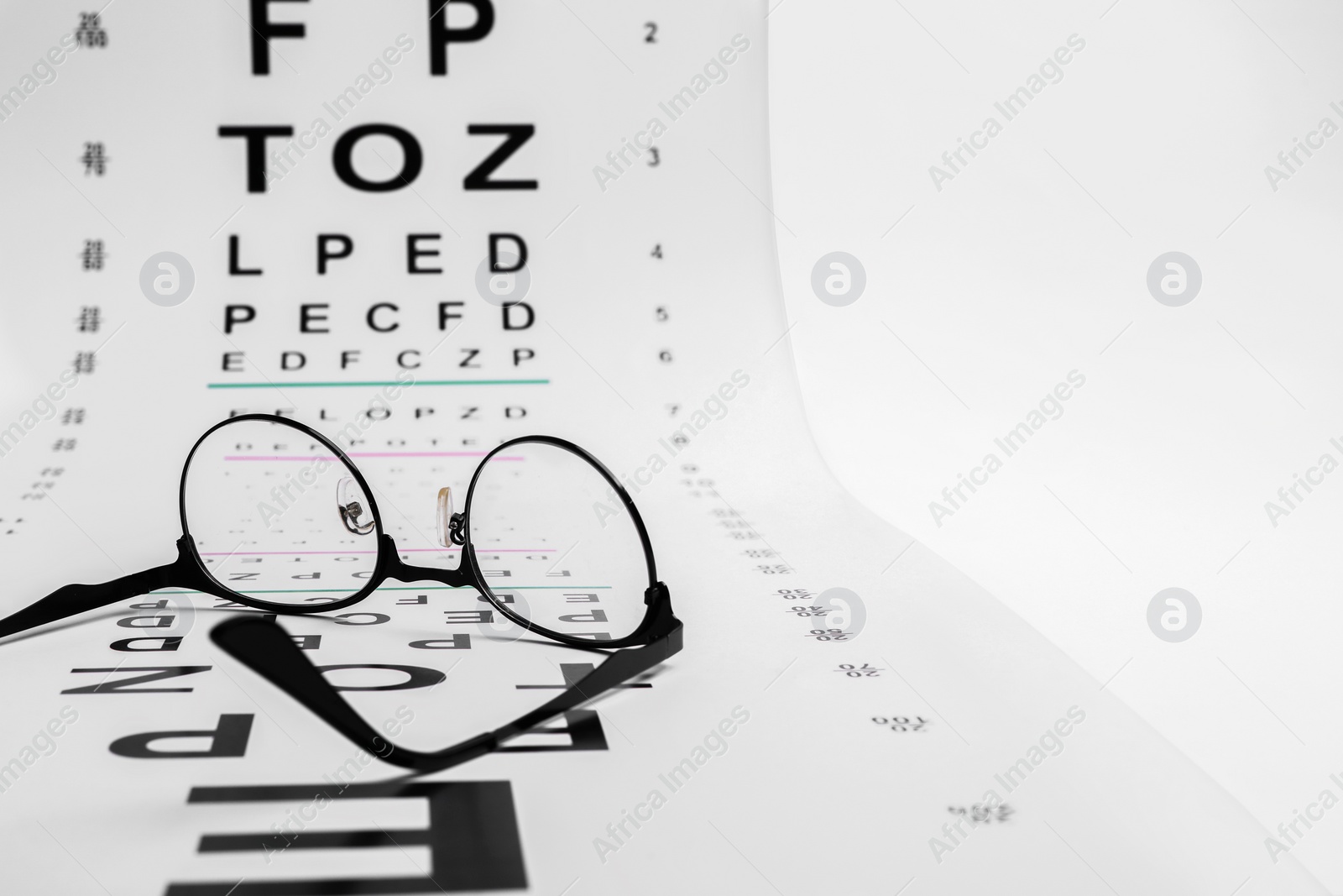 Photo of Vision test chart and glasses on white background, closeup. Space for text