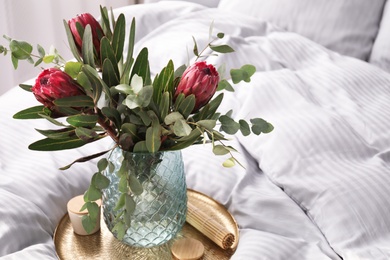 Vase with bouquet of beautiful Protea flowers on bed indoors