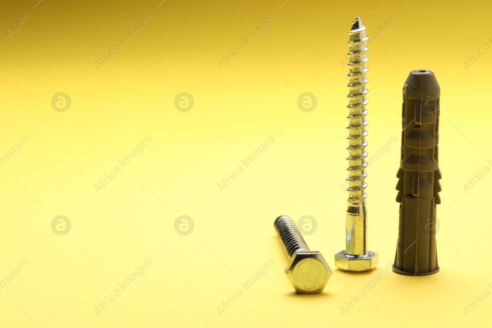 Photo of Self-tapping screw, bolt and dowel on yellow background, space for text