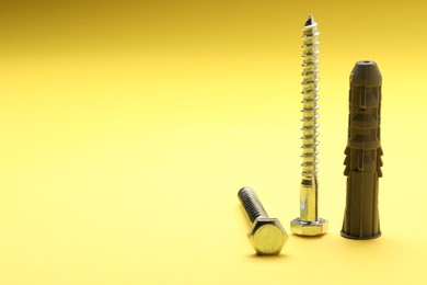 Photo of Self-tapping screw, bolt and dowel on yellow background, space for text