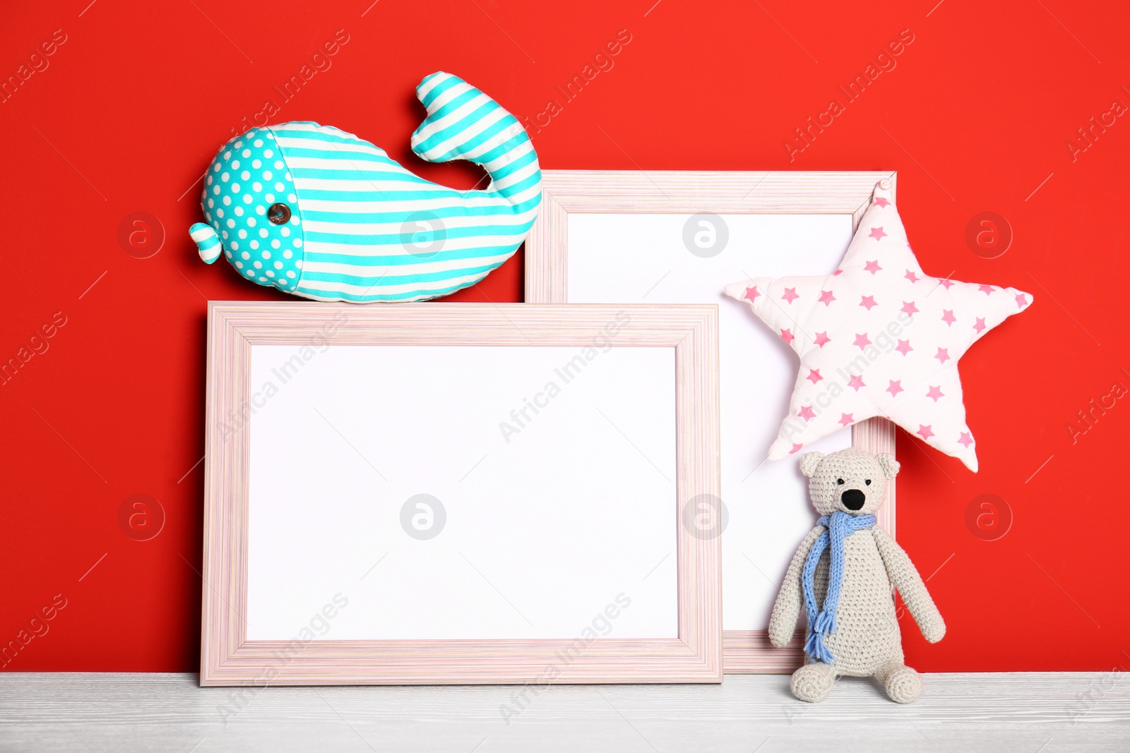 Photo of Soft toys and photo frames on table against red background, space for text. Child room interior