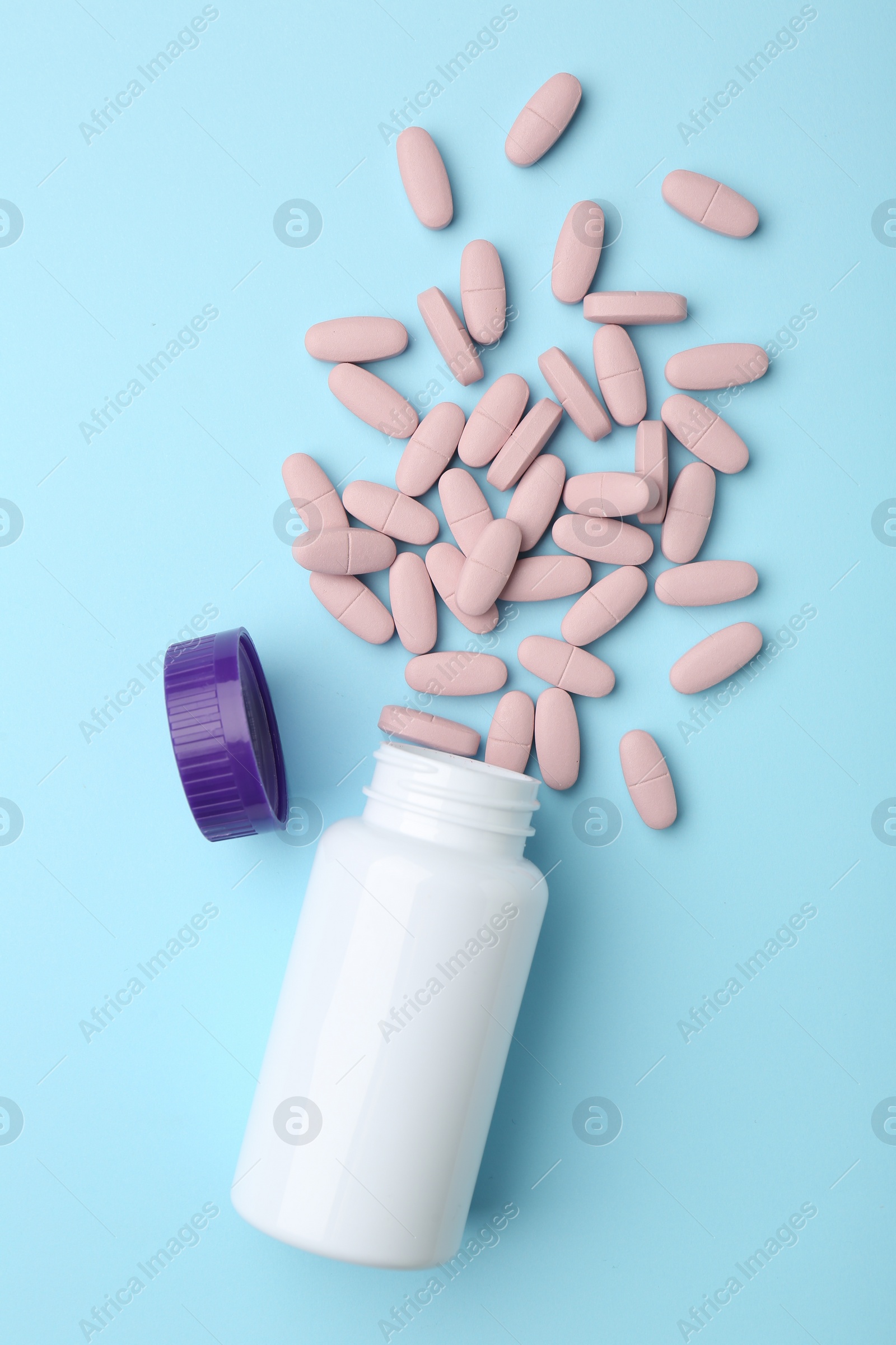 Photo of Vitamin pills, lid and bottle on light blue background, flat lay