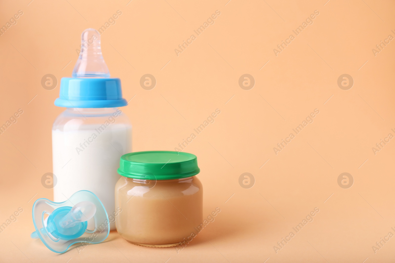 Photo of Healthy baby food, milk and pacifier on pale orange background, space for text