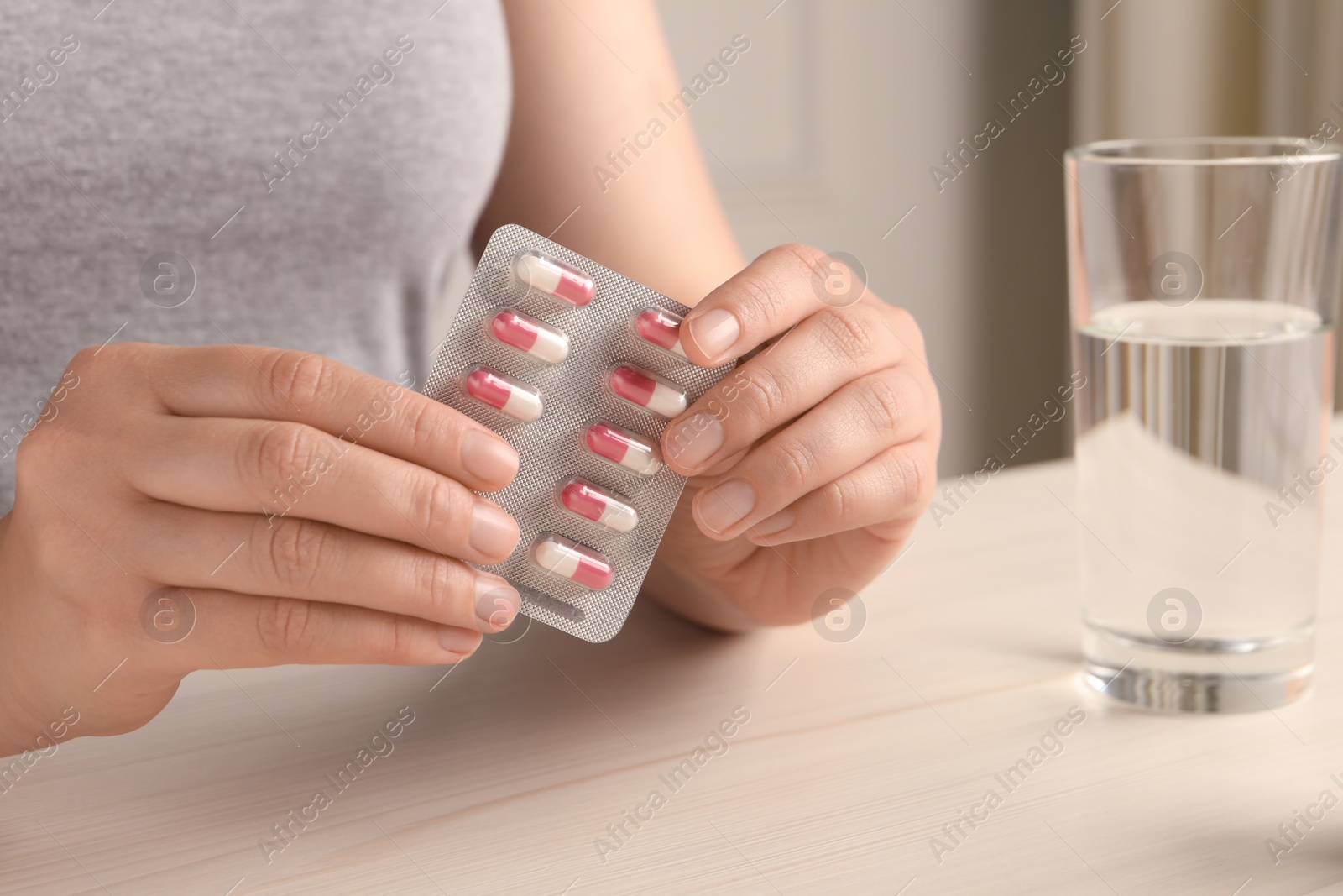 Photo of Woman holding blister of pills at white wooden table, closeup