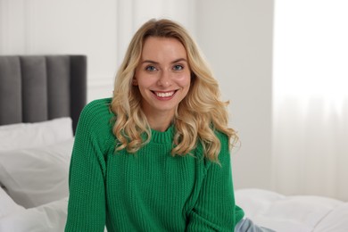 Happy woman in stylish warm sweater on bed at home